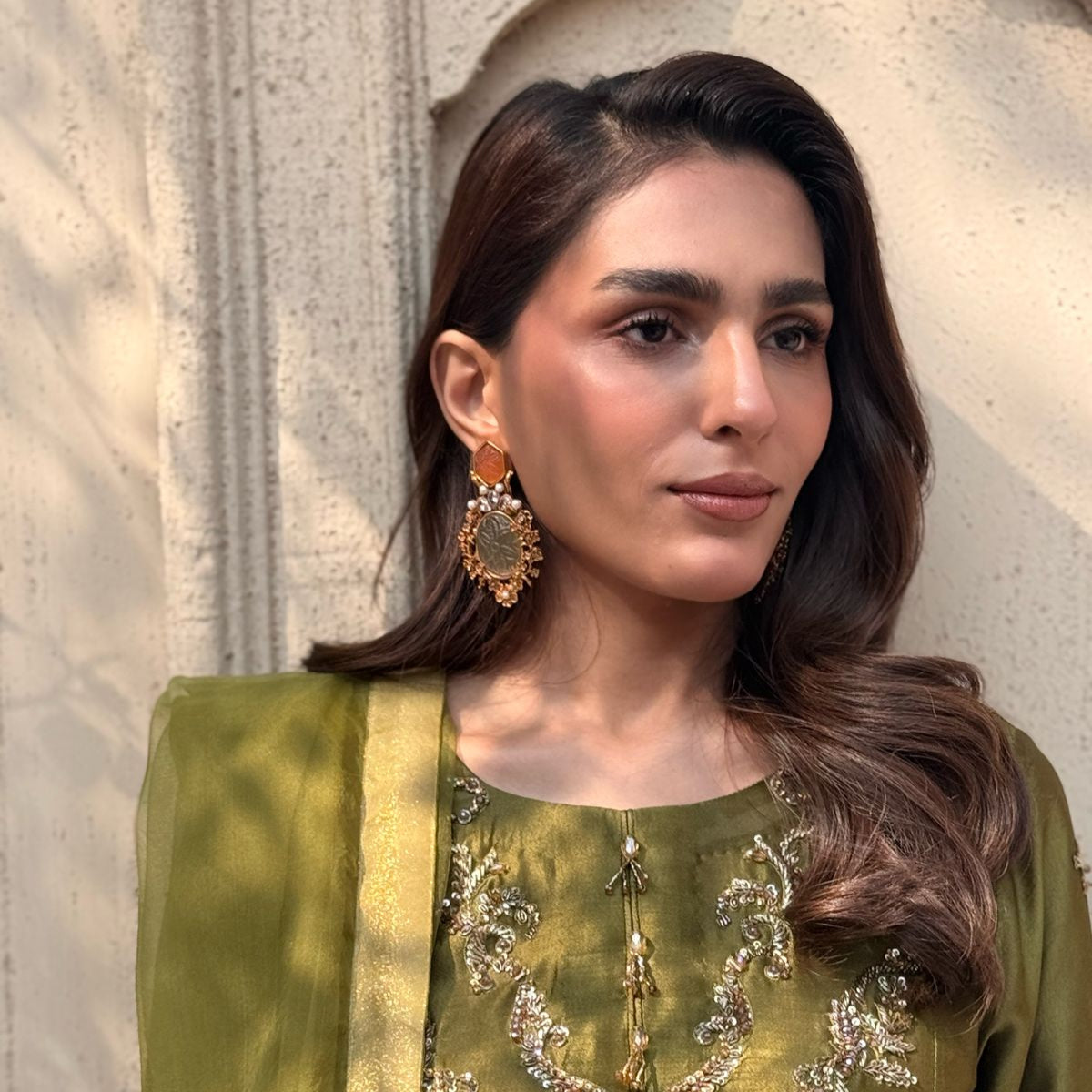 Woman wearing a green traditional outfit with intricate designs and jewelry against a neutral background