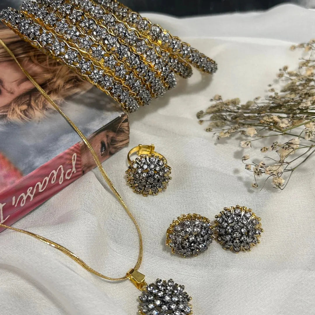 Gold and crystal jewelry set including necklace and earrings on a white surface with dried flowers.