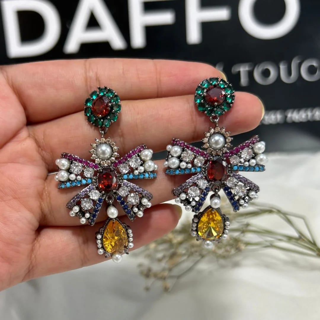 Colorful bow-shaped earrings held in a hand with a blurred background