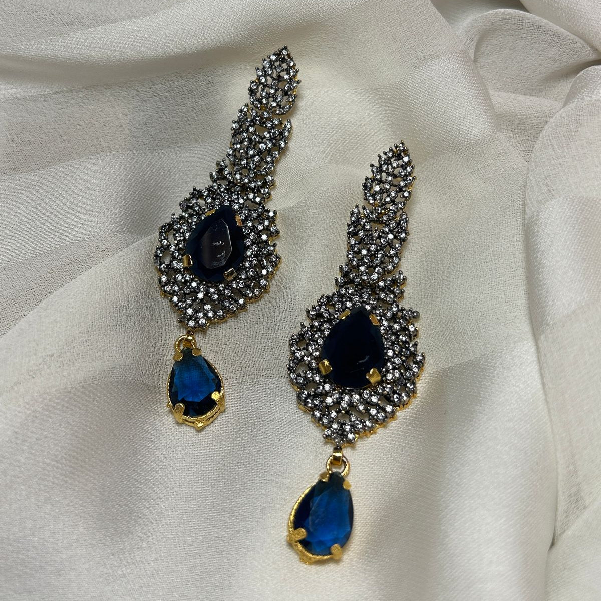 Pair of ornate earrings with blue gemstones on a white fabric background