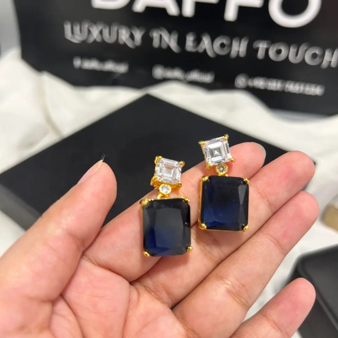 Gold and blue gemstone earrings held in a hand with a DAPPO branded background.