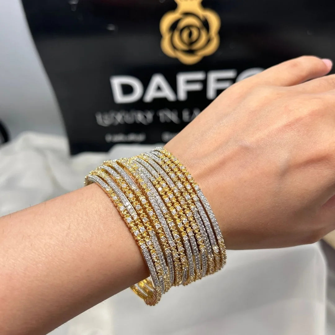 Close-up of a wrist wearing multiple gold and silver bracelets with a brand logo in the background.