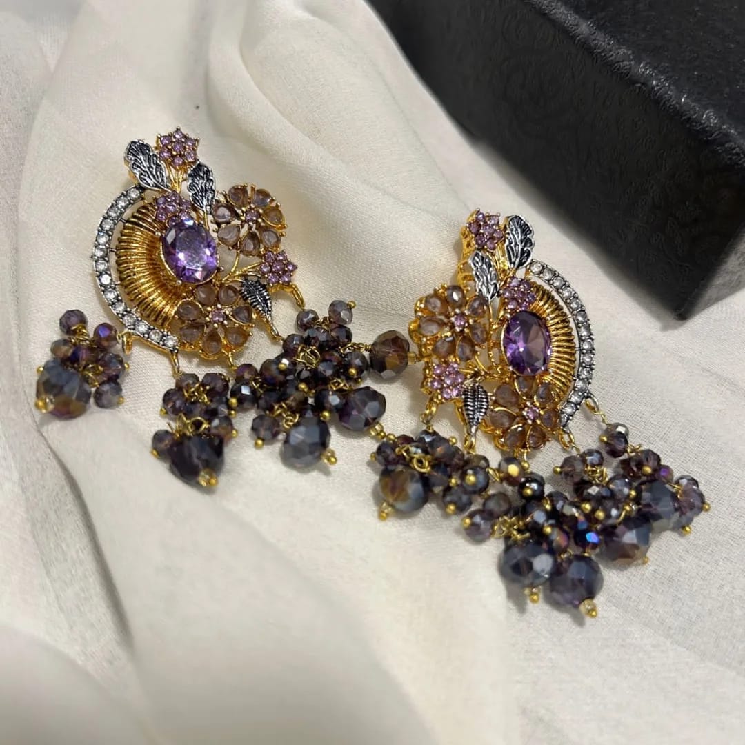 Ornate earrings with purple stones on a white fabric background