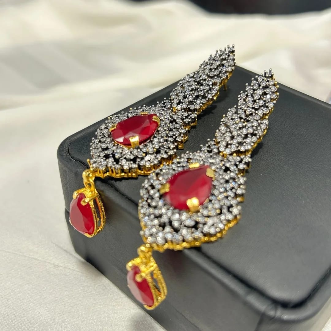 Ornate earrings with red gemstones and gold accents on a black box.