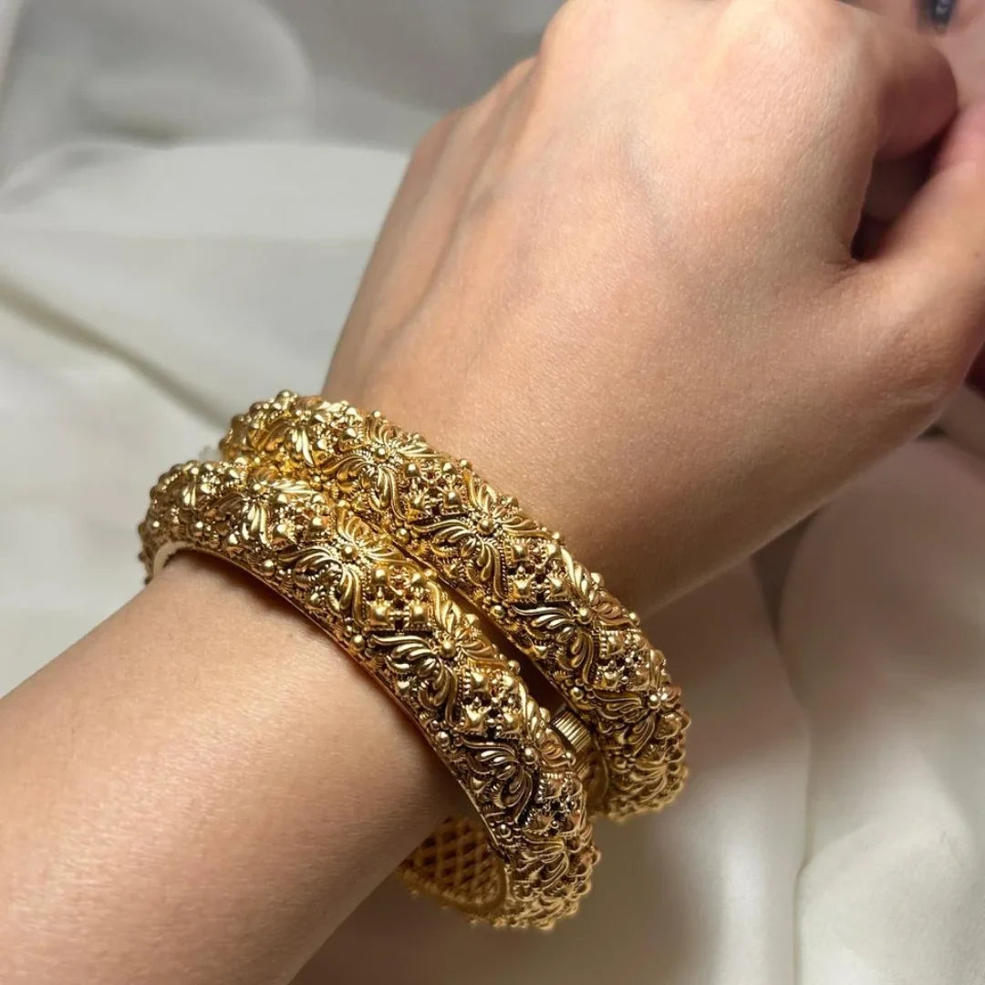 Gold bracelet with intricate design on a wrist against a white background