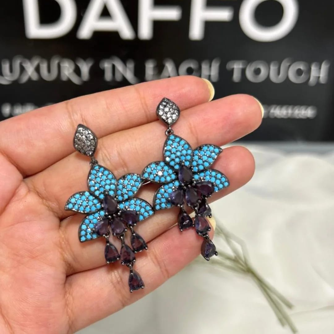 Blue floral earrings held in a hand with a blurred background