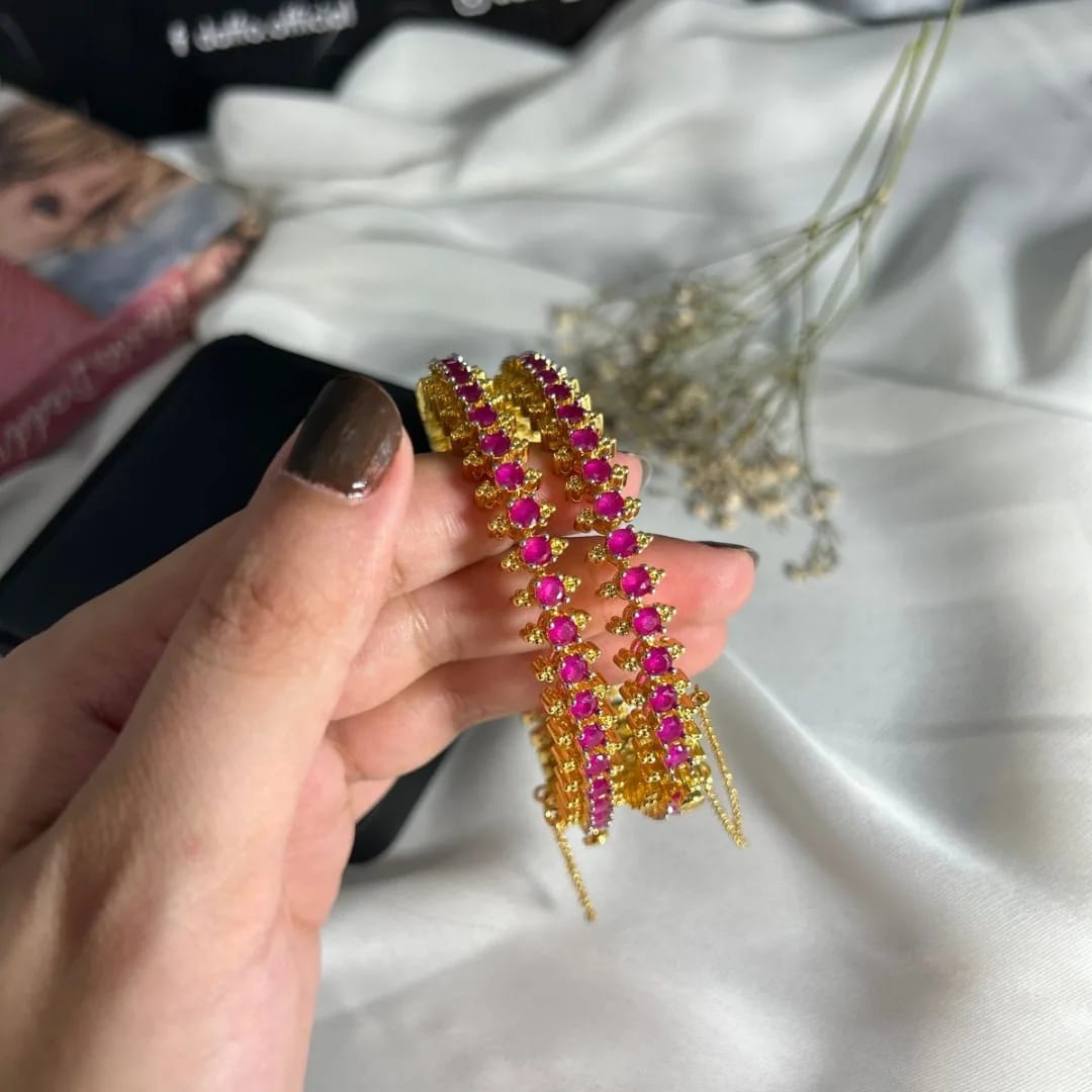 Gold and pink gemstone brooch held by a hand on a light fabric background