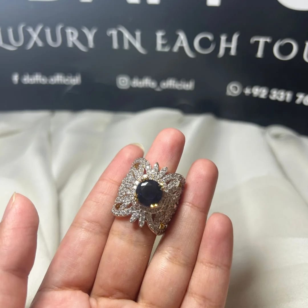 Elegant ring with a dark gemstone on a hand, with a blurred background featuring text. goldplated designer adjustable ring 