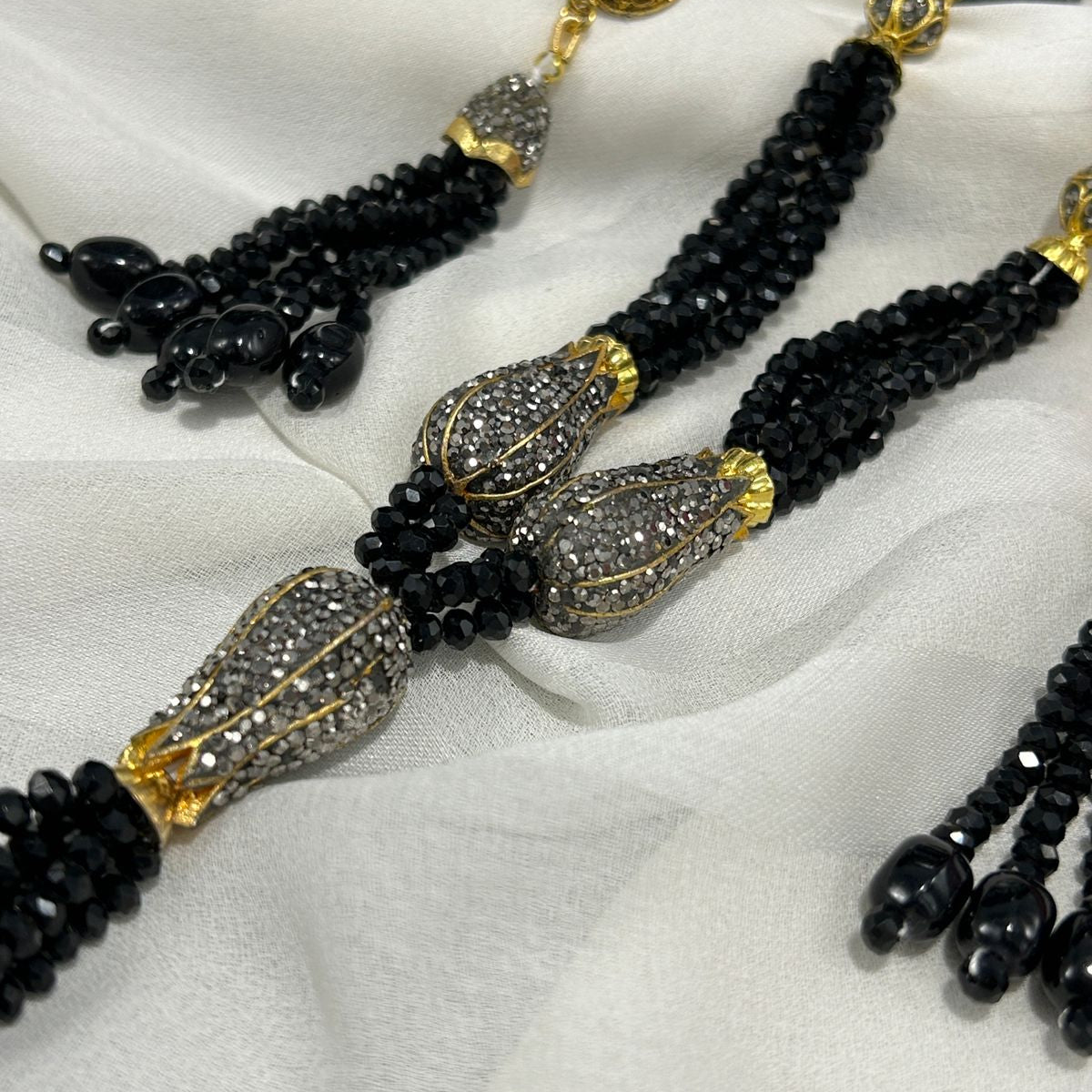 Black beaded necklace with gold and silver accents on a white fabric background