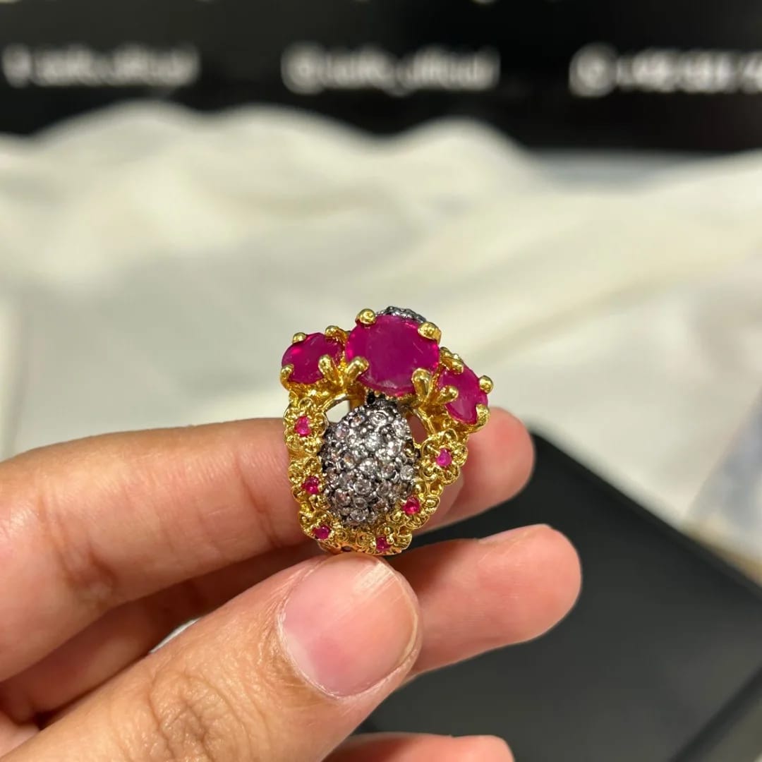 Gold and pink gemstone ring held in a hand with a blurred background