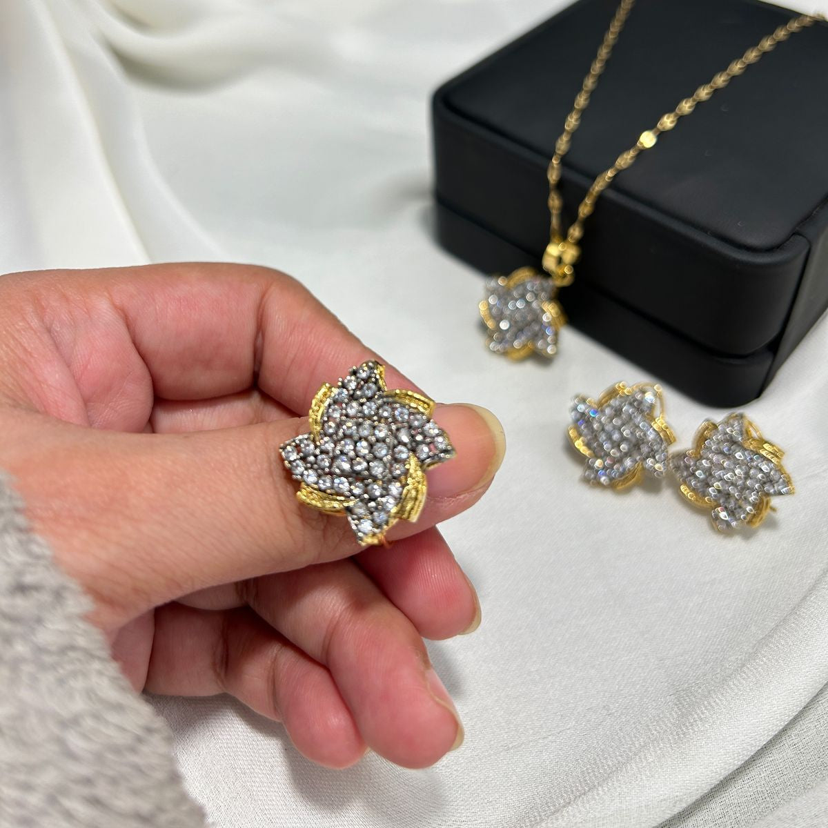Gold and diamond jewelry set with a hand holding an earring, displayed against a branded background.